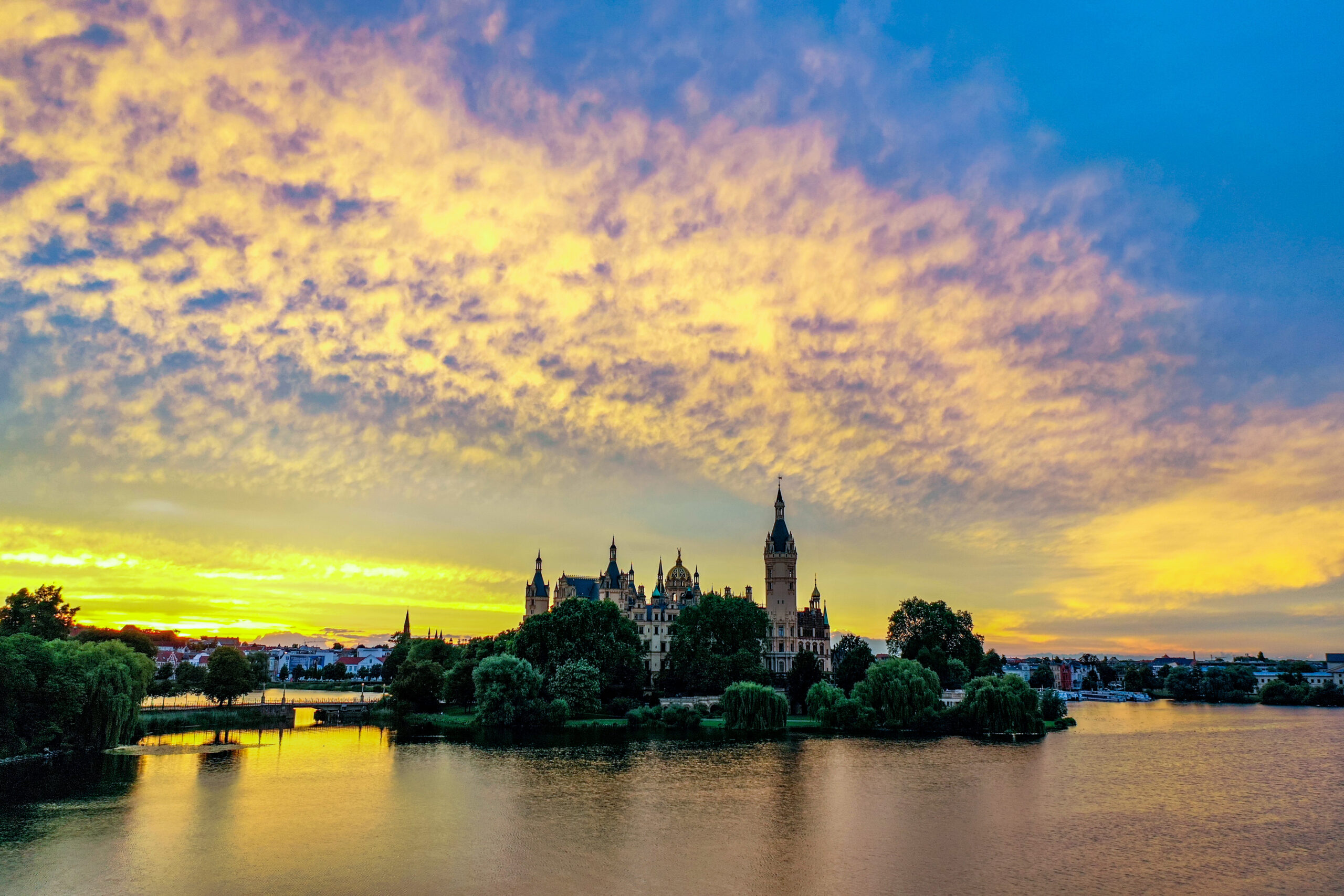 Schwerin von oben 5 a castle on a lake with trees and a sunset