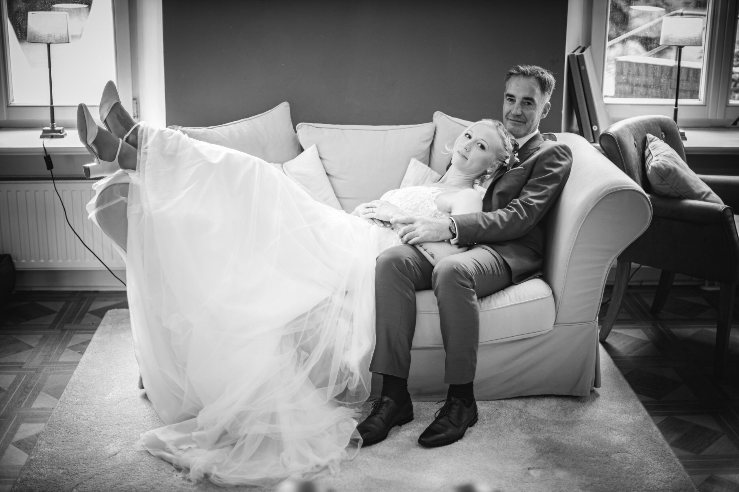 754A3519-66 Hochzeitsfoto auf Schloss Gahmel – Brautpaar entspannt auf dem Sofa in eleganter Schwarzweißaufnahme