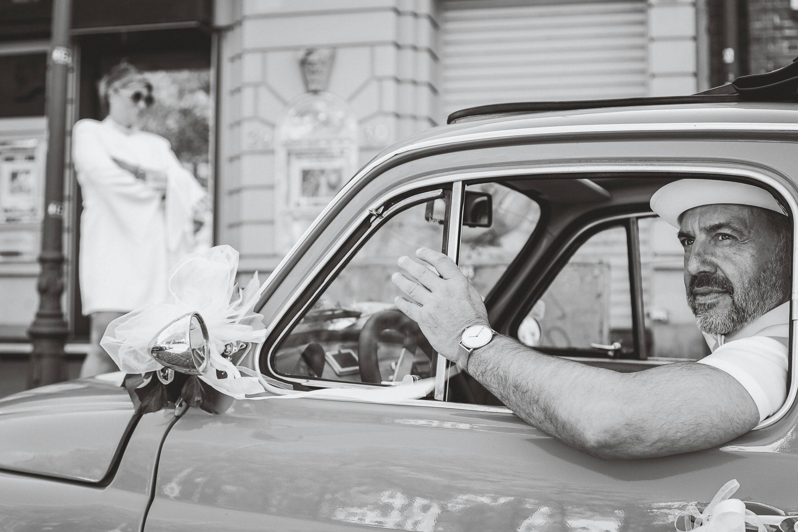 Hochzeitsportraet-Schwarz-Weiss-Editorial-Oldtimer-Eleganz Elegantes Hochzeitsporträt im Schwarz-Weiß-Editorial-Stil. Detailaufnahme des Bräutigams im Oldtimer, das Styling, Komposition und zeitlose Ästhetik betont. Foto aufgenommen auf der Reeperbahn in Hamburg.