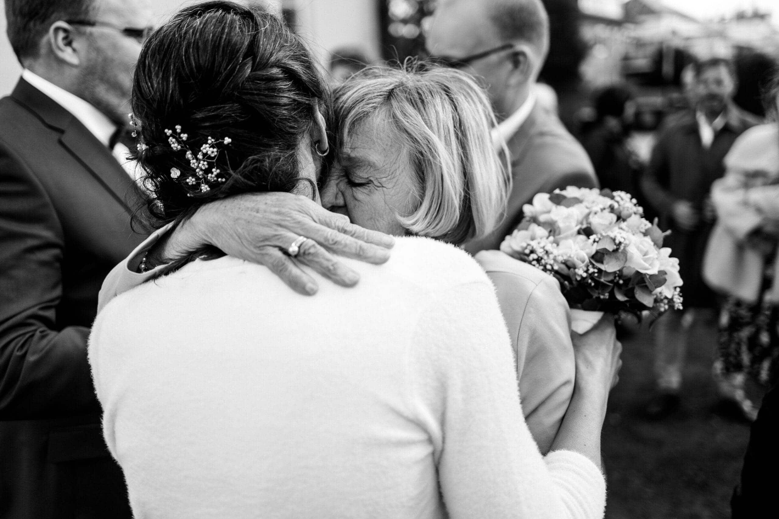 Schwarz-Weiß-Aufnahme einer innigen Umarmung zwischen der Braut und einer älteren Frau, vermutlich ihrer Mutter. Ein sehr emotionaler und liebevoller Moment nach der Trauung.