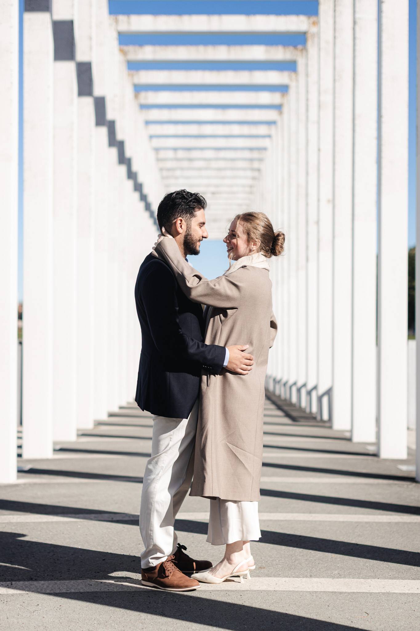 verlobungsshooting-schwerin-pergola-berta-klingberg-platz Ein Paar umarmt sich in der modernen, weißen Säulen-Pergola am Berta-Klingberg-Platz in Schwerin.