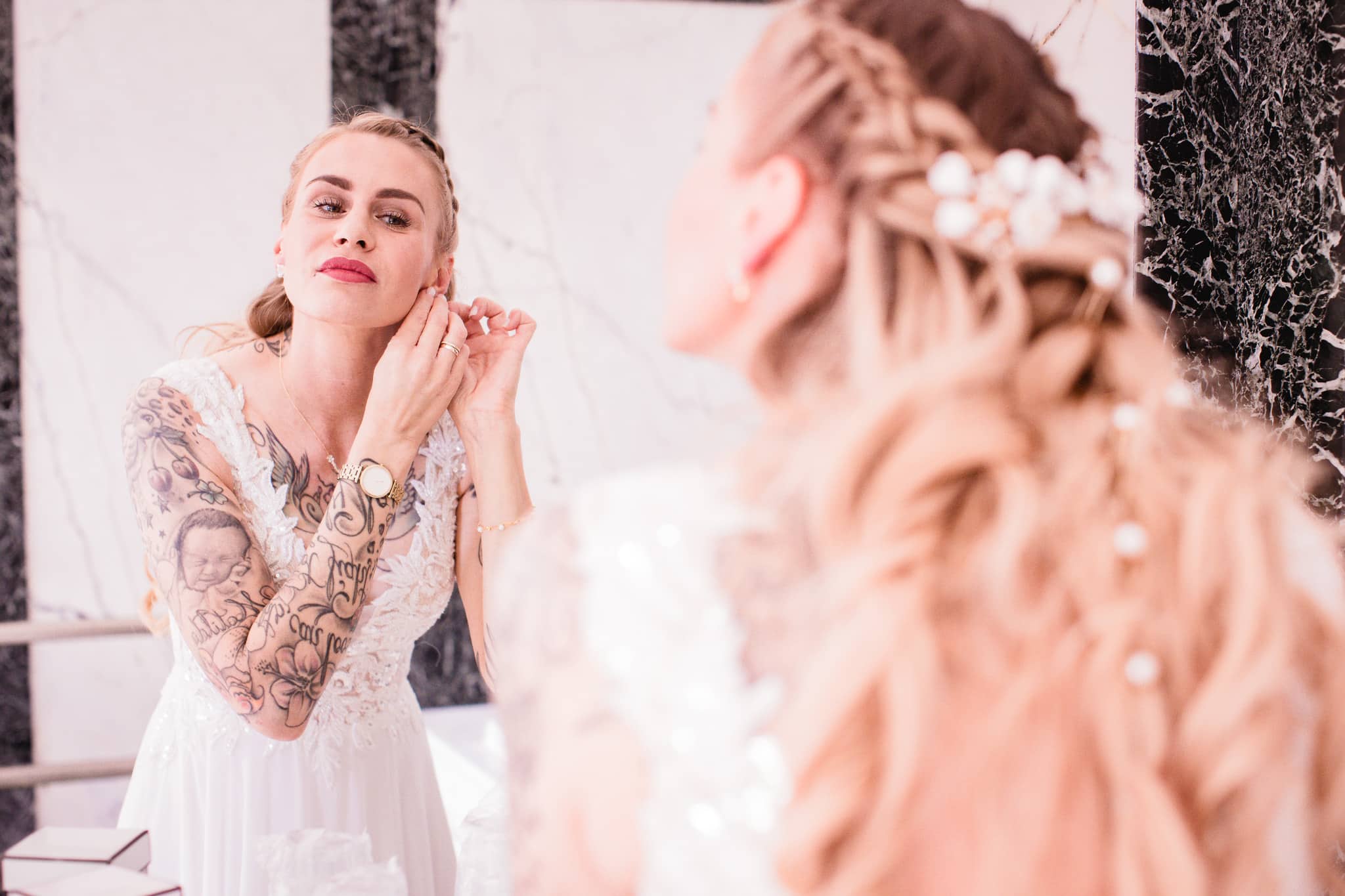 Braut mit Brautkleid und Tattoos legt sich vor einem Spiegel im Schloss Hasenwinkel Ohrringe an beim Getting Ready