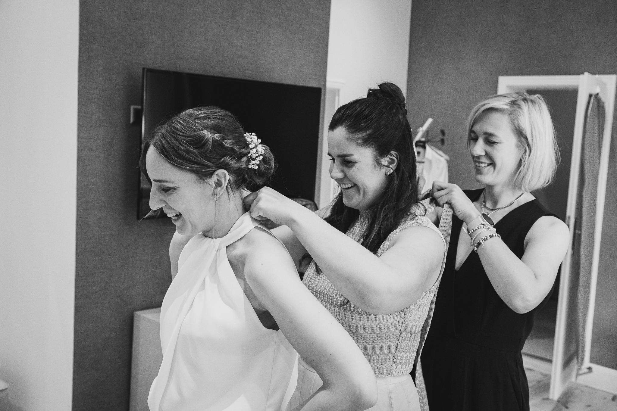Braut wird im Jagdschloss Friedrichsmoor von zwei Freundinnen beim Anziehen des Hochzeitskleides unterstützt – authentischer Moment der Hochzeitsvorbereitung