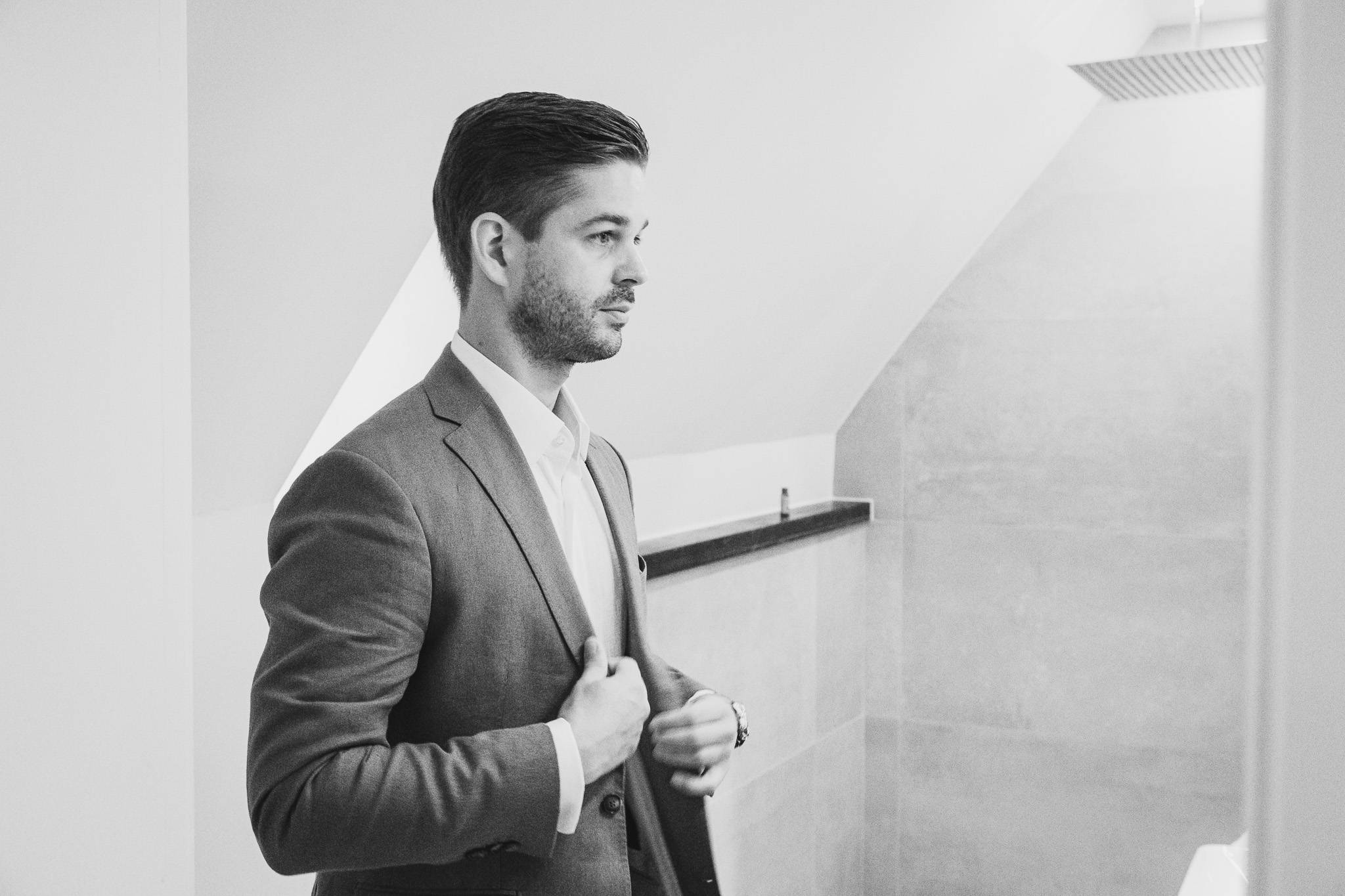 Bräutigam richtet seinen Anzug vor der Hochzeit – klassisches Schwarz-Weiß-Foto der Vorbereitung im modernen Ambiente